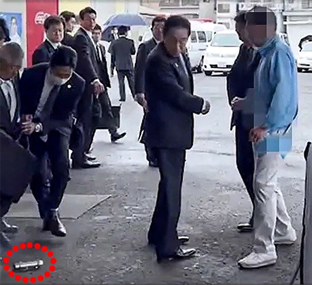 기시다 바로 뒤에 폭탄 15일 오전 11시 26분경 일본 와카야마현 와카야마시 사이카자키 어항의 중의원 보궐선거 유세장을 찾은 기시다 후미오 총리(가운데)가 고개를 돌려 등 뒤쪽 바닥에 떨어진 쇠파이프 모양의 폭발물(점선 안)을 쳐다보고 있다. 경호원(왼쪽에서 두 번째)은 이 폭발물이 날아오다가 땅에 떨어져 기시다 총리 왼발 옆 약 30cm 거리까지 굴러오자 방탄 커버로 쳐낸 뒤 총리를 에워싸고 피신시켰다. 폭발물은 52초 뒤 ‘펑’ 소리를 내며 흰 연기를 내뿜었다. 산케이뉴스 유튜브 캡처