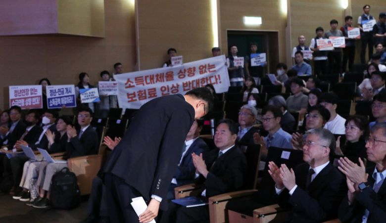 국민연금 재정계산위원회 공청회 1일 서울 강남구 코엑스에서 열린 국민연금 재정계산위원회의 공청회에서 이기일 보건복지부 1차관이 참석자들에게 인사하고 있다. 그  뒤에는 위원회가 제시한 연금개혁 방안에 반대하는 집회 참가자들이 ‘소득대체율 상향 없는 보험료 인상 반대한다’ 등의 문구가 적힌  피켓, 현수막을 들고 있다. 복지부는 의견 수렴을 거쳐 10월까지 국민연금 개혁 방안인 종합운영계획을 마련할 예정이다. 뉴시스