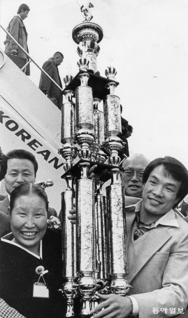 1977년 11월  파나마에서 열린 WBA 주니어 페더급 초대 챔피언결정전에서 헥토르 카라스키야(파나마)를 맞아 2라운드 4차례 다운을 당했지만 3라운드 기적같은 KO승을 거두고 두 번째 세계 챔피언 자리에 오른 홍수환이 트로피를 들고 귀국 비행기에서 내리고 있다. 동아일보 DB