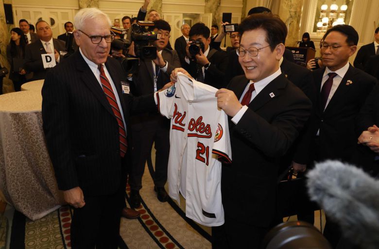 이재명 대통령이 25일(현지시간) 미국 워싱턴DC 윌라드 호텔에서 열린 한미 비즈니스 라운드 테이블 리셉션에 참석해 미국 칼라일 그룹 데이비드 루벤스타인 공동회장(왼쪽)으로부터 이 대통령 이름이 새겨진 메이저리그 볼티모어 오리올스 유니폼을 선물받고 있다. 2025.8.26 대통령실사진기자단