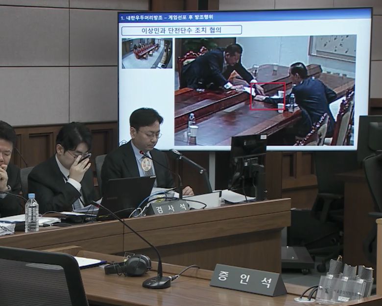 2025년 10월 13일 서울중앙지법 형사합의33부(부장판사 이진관) 심리로 열린 한덕수 전 국무총리 2차 공판에서 특검이 제시한 12·3 비상계엄 당일 대통령실 폐쇄회로(CC)TV 영상 화면에 한 전 총리(오른쪽)와 이상민 전 행정안전부 장관이 계엄 관련 문건을 주고받고 있는 모습이 재생되고 있다. 법원 공판 중계 화면 캡처