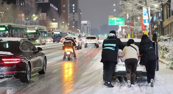 서울·인천·경기·강원 등 4개 시도에 대설특보가 발효된 4일 서울 마포구 홍대 인근에서 제설작업이 완료되지 못한 도로에서 시민들이 언덕길 차를 밀고 있다. 그 옆으로는 빙판이 된 도로 위로 차와 오토바이가 지나고 있다. 〈사진=연합뉴스〉