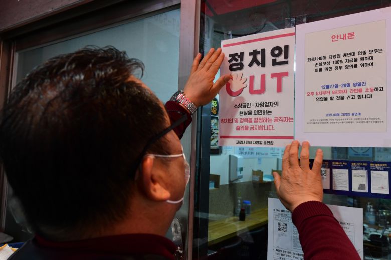 22일 서울 시내의 한 식당가에서 코로나피해자총연합회 회원이 '정치인 출입 금지' 안내문을 붙이고 있다.