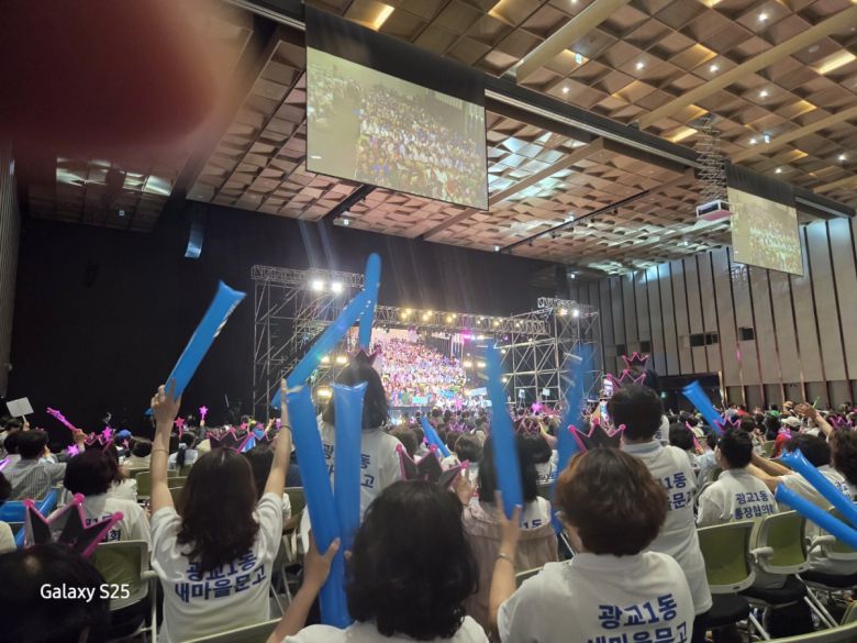 13일 수원컨벤션센터에서 열린 ‘2025 새빛 힐링콘서트’에서 수원시 봉사자들이 단체 티셔츠와 핑크색 왕관 머리띠를 착용하고 파란 풍선을 흔들며 무대 공연을 관람하고 있다.