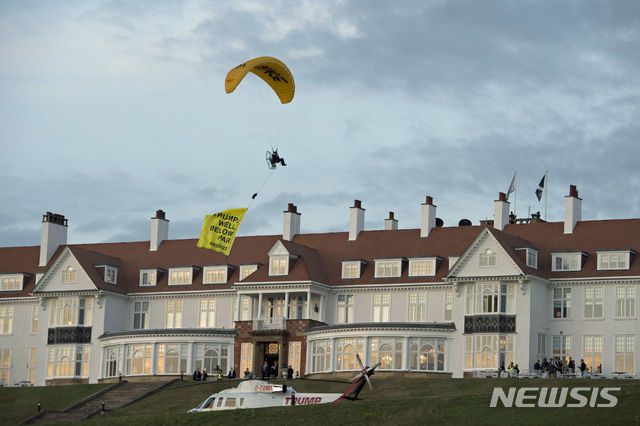 【턴베리(스코틀랜드)=AP/뉴시스】도널드 트럼프 미국 대통령이 2018년 7월14일(현지시간) 영국 스코틀랜드 텐베리에 위치한 턴베리 호텔에 방문한 가운데, 이에 앞서 13일 한 시위대가 패러글라이를 타고 호텔 상공에서 트럼프의 방문에 반대하는 시위를 벌이고 있다. 그는 그린피스소속으로, 패러글라이등 배너에는 "트럼프: 수준이하"라고 적혔다. 20118.07.15.