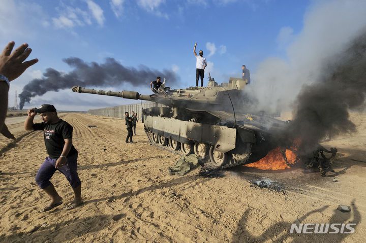 [칸유니스=AP/뉴시스] 2023년 10월 7일(현지 시간) 팔레스타인 칸유니스 인근 가자지구에서 팔레스타인 주민들이 파괴된 이스라엘 전차 주변에 몰려들어 환호하고 있다. 2025.10.08.