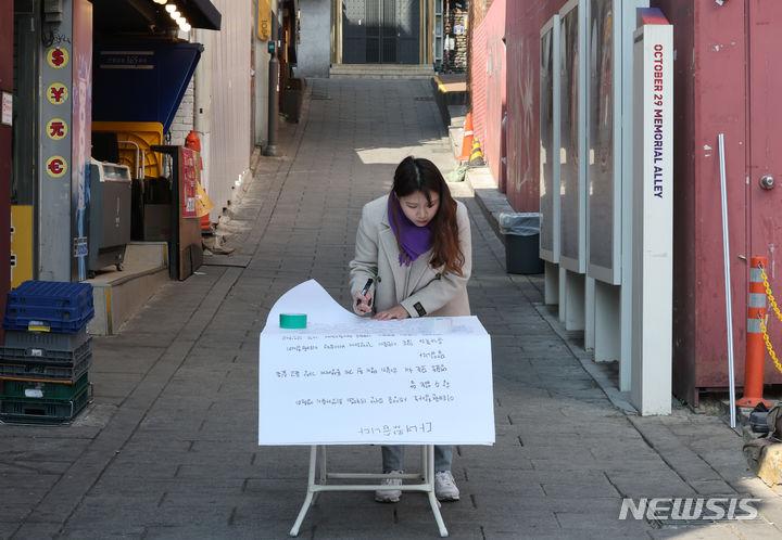[서울=뉴시스] 김진아 기자 = 21일 서울 이태원역 1번 출구 앞 이태원참사 추모의 벽에서 10.29 이태원참사 희생자 유연주의 언니 유정이 2030 세대에게 호소하는 대자보를 작성하고 있다.  2024.03.21. bluesoda@newsis.com