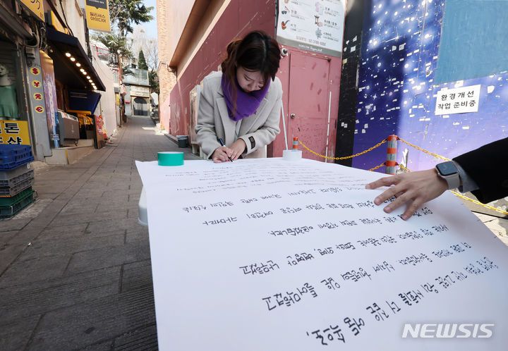 [서울=뉴시스] 김진아 기자 = 21일 서울 이태원역 1번 출구 앞 이태원참사 추모의 벽에서 10.29 이태원참사 희생자 유연주의 언니 유정이 2030 세대에게 호소하는 대자보를 작성하고 있다.  2024.03.21. bluesoda@newsis.com