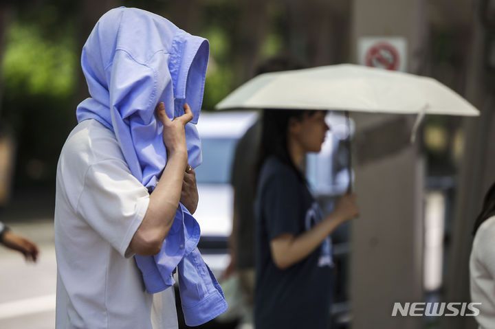 [서울=뉴시스] 정병혁 기자 = 서울을 비롯한 대부분의 지역에 폭염주의보가 발령된 19일 서울 영등포구 여의도환승센터에서 한 시민이 옷으로 햇빛을 가린 채 이동하고 있다. 2024.06.19. jhope@newsis.com