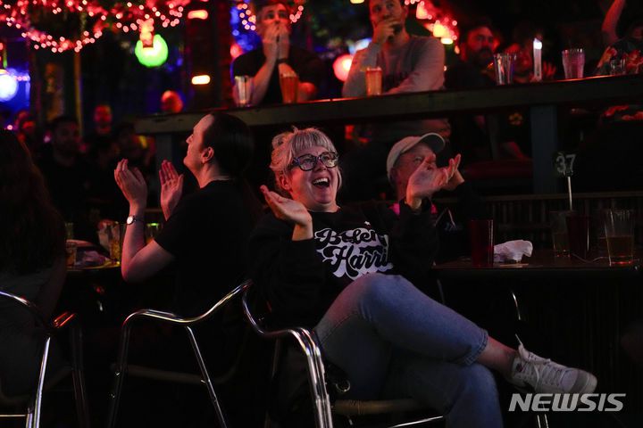 [시애틀=AP/뉴시스] 27일(현지시각) 미 워싱턴주 시애틀의 한 술집에서 바이든·해리스 티셔츠를 입은 애이미 포팅어라는 여성이 2021년 1월 6일 도널드 트럼프 당시 대통령이 연방 의회 난입에 어떻게 대처했는지 언급하는 TV 토론 속 조 바이든 대통령을 보며 박수하고 있다. 2024.06.28.