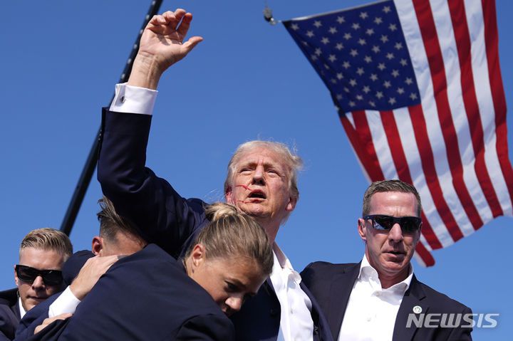 [버틀러(미 펜실베이니아주)=AP/뉴시스] 도널드 트럼프 전 미국 대통령이 지난 해 7월 13일  펜실베이니아주 버틀러에서 대선 유세 도중 암살시도 총격을 당한 직후 경호원들에게 둘러싸여 연단을 내려오면서 오른쪽 귀에 피를 흘리는 상태로 주먹을 흔들며 "싸우자"고 외치고 있다. 2025.05.06.