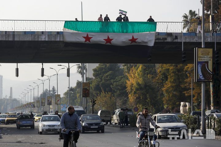 [다마스쿠스=AP/뉴시스] 12월 9일  시리아 다마스쿠스에서 시민들이 육교에 시리아 반군 깃발을 내걸고 흔들며 바샤르 알아사드 정권의 붕괴를 축하하고 있다. 2024.12.11.