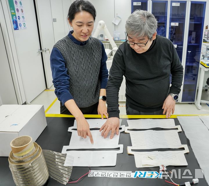 [창원=뉴시스]한국전기연구원(KERI) 이동윤(오른쪽) 박사가 동료 연구원과 고효율 고유연 ‘금속섬유천 면상 발열체’ 상태를 살펴보고 있다.(사진=한국전기연구원 제공) 2025.01.14.photo@newsis.com