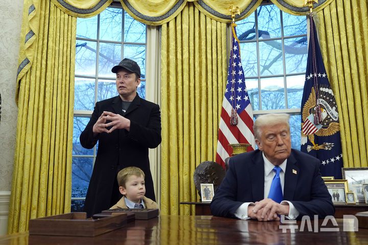 [워싱턴=AP/뉴시스] 일론 머스크가 11일(현지 시간) 워싱턴DC 백악관 대통령 집무실에서 발언하고 있다. 아래는 머스크 아들 엑스 애쉬 에이 트웰브(X Æ A-Xii), 오른쪽은 도널드 트럼프 미국 대통령. 2025.02.12.