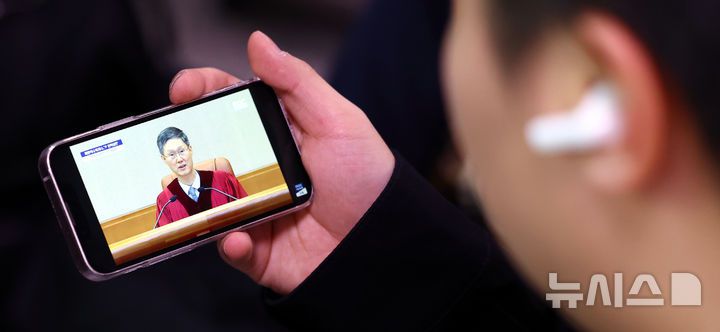 [서울=뉴시스] 박주성 기자 = 4일 오전 서울 용산구 서울역 역사에서 시민이 핸드폰으로 윤석열 대통령 탄핵심판 선고를 시쳥하고 있다. 2025.04.04. park7691@newsis.com