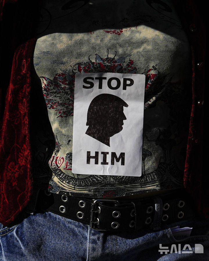 [뉴욕=AP/뉴시스] 지난 17일(현지 시간) 미국 뉴욕 폴리 광장에서 열린 '고등교육 행동의 날' 시위 중 한 시민이 도널드 트럼프 대통령 옆모습이 그려진 스티커를 셔츠에 붙이고 있다. 2025.04.30.