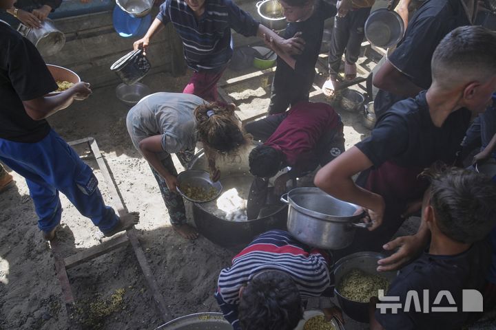 [칸유니스=AP/뉴시스]  가자지구 남부 칸유니스에서 음식 배급이 끝난 뒤 팔레스타인 어린이들이 배급 용기에 남은 음식을 긁어모으고 있다. 가자 보건부는 최근 어린이 뇌막염 환자가 급증하고 있다며 지원을 호소했다. 2025.07.09.