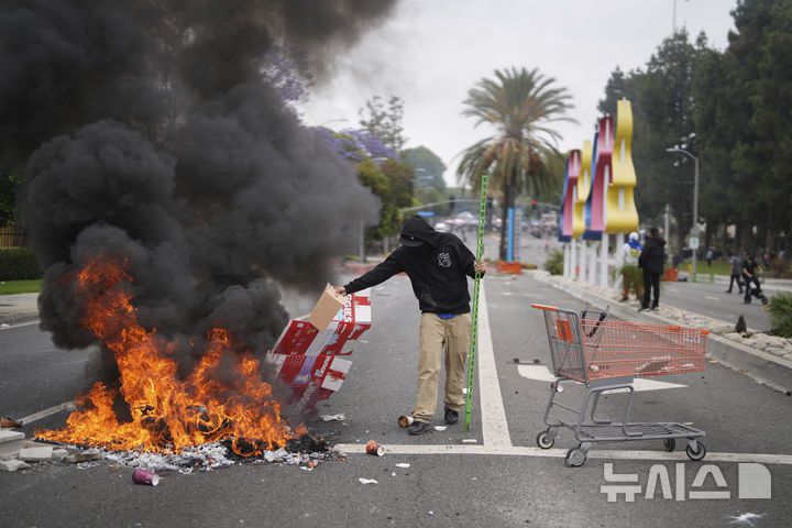 [캘리포니아=AP/뉴시스] 도널드 트럼프 미국 대통령이 이민 단속 시위를 진압하기 위해 캘리포니아주에 주방위군 2000명을 투입하라고 지시하자 "극히 이례적인 조치"라는 평가가 나오고 있다고 뉴욕타임스가 8일(현지 시간) 보도했다. 사진은 7일 캘리포니아 파라모운트의 한 산업 단지 밖에서 방호복과 가스 마스크를 착용한 국경 순찰대 요원들이 경계를 서고 있는 가운데, 한 시위자가 불길에 잡동사니를 넣고 있다. 2025.06.08.
