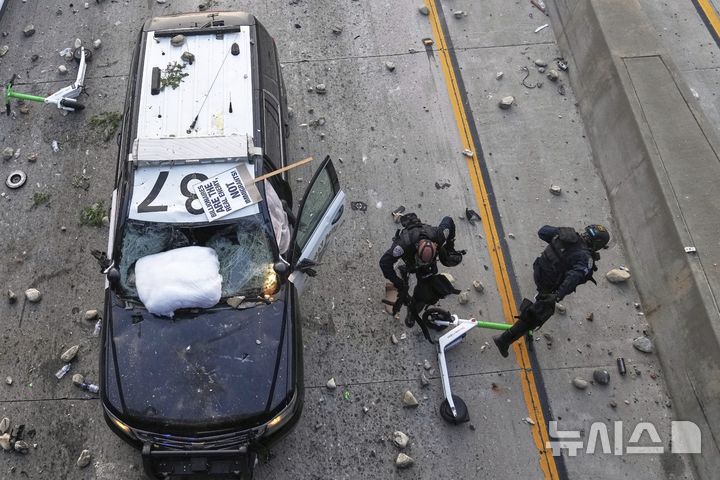 [로스앤젤레스=AP/뉴시스] 8일(현지 시간) 미 캘리포니아주 로스앤젤레스 도심 메트로폴리탄 구치소 인근 101번 고속도로에서 경찰관 두 명이 이민세관단속국(ICE)의 불법 이민자 단속에 항의해 시위대가 던지는 돌과 스쿠터를 피하고 있다. 2025.06.09.