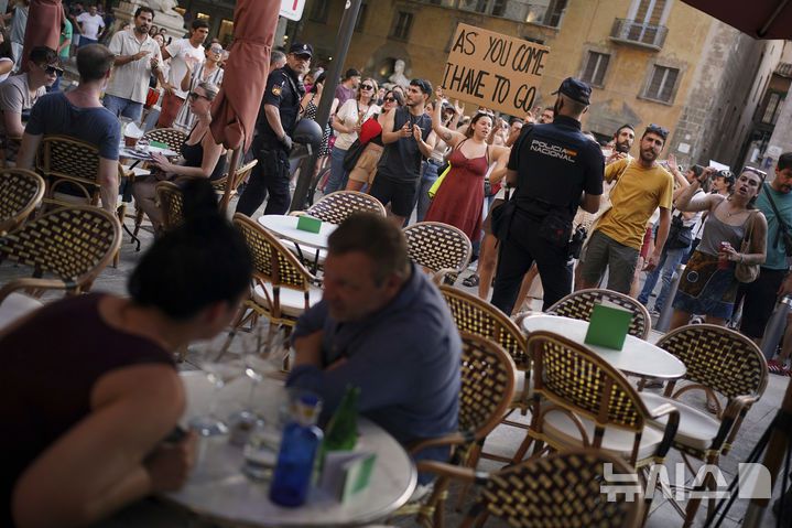 [마요르카=AP/뉴시스] 15일(현지 시간) 스페인 마요르카에서 오버투어리즘(과잉 관광)에 반대하는 시위가 열린 가운데 관광객들이 이를 지켜보고 있다. 2025.06.16.
