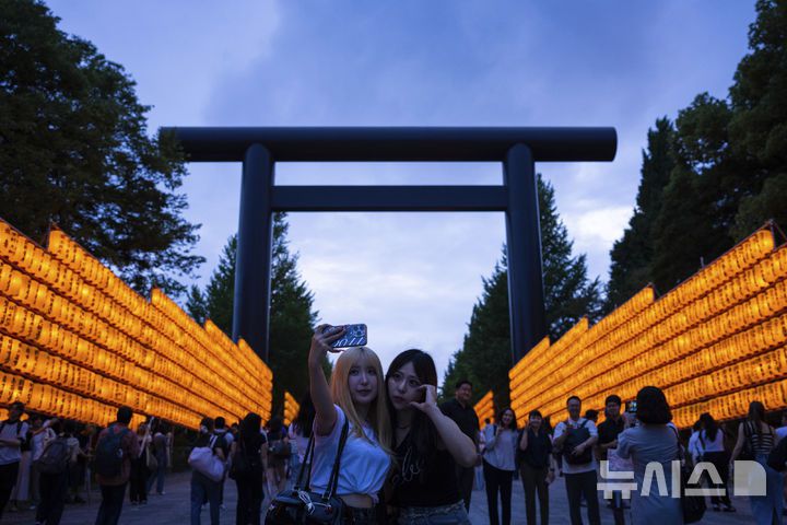 [도쿄=AP/뉴시스] 지난달 16일 일본 도쿄 야스쿠니 신사에서 미타마 마쓰리가 열려 방문객들이 노란색 등불을 배경으로 셀카를 찍고 있다. 2025.08.15.
