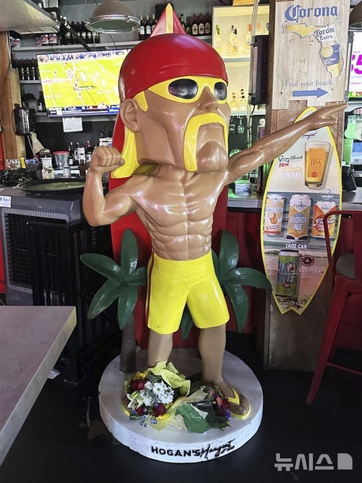 [클리어워터 비치=AP/뉴시스] 24일(현지 시간) 미 플로리다주 클리어워터 비치에 있는 바 겸 레스토랑 '호건스 행아웃' 내부의 호건 동상 밑에 고인의 죽음을 애도하는 꽃다발이 놓여 있다. 미 프로레슬링 전설 헐크 호건(본명 테리 진 볼레아)이 71세를 일기로 별세했다. 사인은 심장마비로 알려졌다. 2025.07.25.