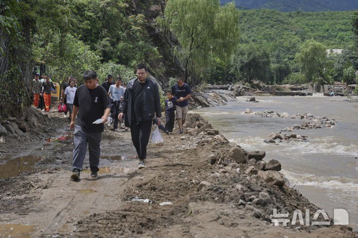 [베이징=AP/뉴시스] 29일(현지 시간) 중국 베이징 교외 미윈구에서 폭우로 홍수 피해를 입은 마을 주민들이 짐을 챙겨 훼손된 도로를 따라 대피하고 있다. 현지 당국은 지난 주말 이후 베이징 전역에 폭우가 쏟아져 미윈구 강수량이 543.4㎜를 기록했고 최소 28명이 숨졌다고 전했다. 2025.07.29.