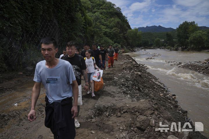 [베이징=AP/뉴시스] 29일(현지 시간) 중국 베이징 외곽 미윈구에서 폭우로 홍수 피해를 입은 랑자위 마을 주민들이 짐을 챙겨 훼손된 도로를 따라 대피하고 있다. 현지 당국은 지난 주말 이후 베이징 전역에 폭우가 쏟아져 미윈구 강수량이 543.4㎜를 기록했고 최소 28명이 숨졌다고 전했다. 2025.07.29.