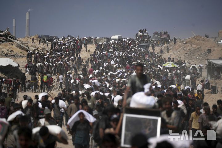 [베이트 라히야=AP/뉴시스] 지난 1일(현지 시간) 가자지구 북부 베이트 라히야 외곽에서 팔레스타인 주민들이 가자시티로 향하던 인도적 물품 수송 트럭에서 내린 밀가루 자루를 나르고 있다. 2025.08.04.