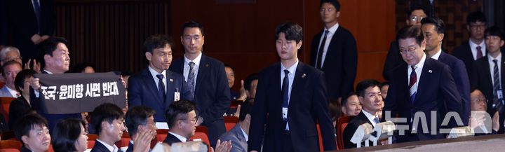 [서울=뉴시스] 최동준 기자 = 이재명 대통령이 15일 서울 종로구 세종문화회관에서 열린 제80주년 광복절 경축식에서 경축사를 마치고 이동하고 있는 가운데 안철수 국민의힘  당대표후보가 조국, 윤미향 사면 반대 피켓을 들고 있다. 2025.08.15. photocdj@newsis.com