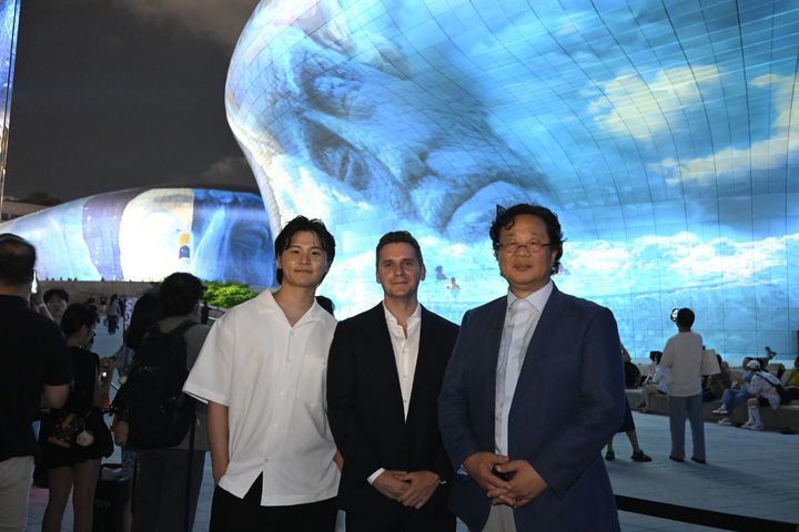 [서울=뉴시스] 오픈AI가 서울디자인재단과 협력해 세계 최대 규모의 비정형 건축물 3D 미디어 파사드 축제인 '서울라이트 DDP 2025 가을'에 참여했다. 오픈AI 지원을 받은 최세훈 작가(왼쪽)가 인공지능(AI) 영상 생성 도구 '소라'로 제작한 미디어 아트 'The Valley and the light' 앞에서 제이크 윌크진스키 오픈AI 아시아태평양 지역 커뮤니케이션 총괄(가운데)과 최강희 서울디자인재단 대표이사와 함께 기념사진을 찍었다. (사진=최세훈 작가 제공) *재판매 및 DB 금지