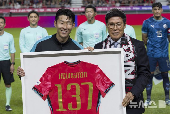 [서울=뉴시스] 김근수 기자 = 한국 남자 선수 A매치 최다 출전한 손흥민이 14일 오후 서울 마포구 서울월드컵경기장에서 열린 하나은행 초청 축구국가대표팀 친선경기 대한민국과 파라과이의 경기 시작 전 차범근 전 감독에게 기념 유니폼을 전달받고 기념촬영을 하고 있다.손흥민은 지난 10일 브라질전에 개인 통산 137번째 A매치에 출전했다.  차범근 전 대표팀 감독, 홍명보 대표팀 감독(이상 136경기)을 제치고 한국 남자 축구 역사상 최다 출전 기록 보유자가 됐다. 2010년 12월 시리아전 데뷔 이후 15년 만이다.  2025.10.14. ks@newsis.com