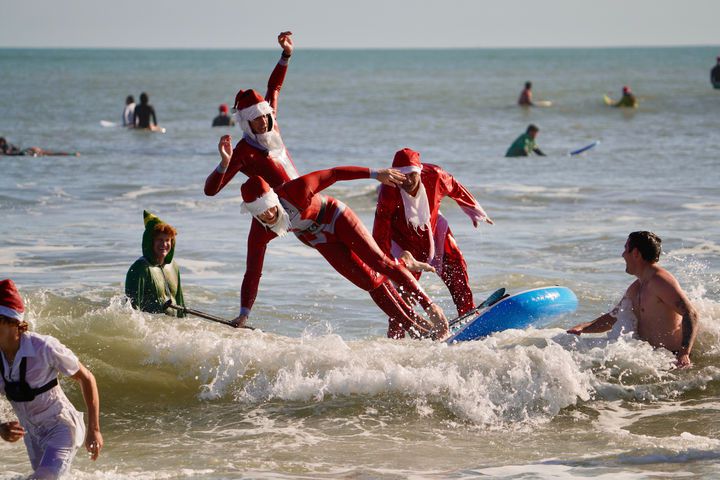 [코코아비치=AP/뉴시스] 24일(현지 시간) 미 플로리다주 코코아비치에서 크리스마스이브를 맞아 열린 연례 ‘서핑 산타’ 행사에서 산타 복장의 참가자들이 파도를 타고 있다. 2025.12.25.