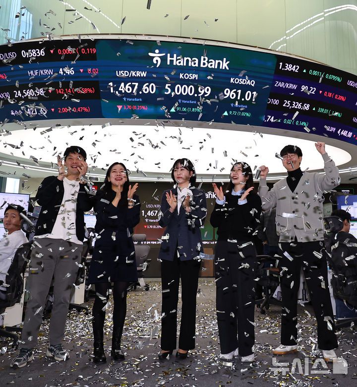 [서울=뉴시스] 최진석 기자 = 코스피가 꿈의 숫자로 여겨지던 '오천피'에 도달하며 코스피 5000 시대가 열린 22일 오전 서울 중구 하나은행 딜링룸에서 관계자들이 코스피 5000 돌파를 축하하고 있다. 코스피는 전 거래일(4909.93)보다 77.13포인트(1.57%) 상승한 4987.06에 개장했다.2026.01.22. myjs@newsis.com