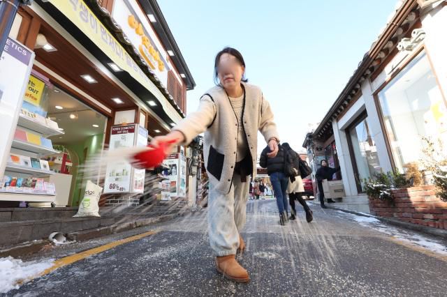 A shop owner spreads calcium chloride on an icy road in Bukchon, Jongno District, Seoul, on December 5, 2025. AJP Han Jun-gu