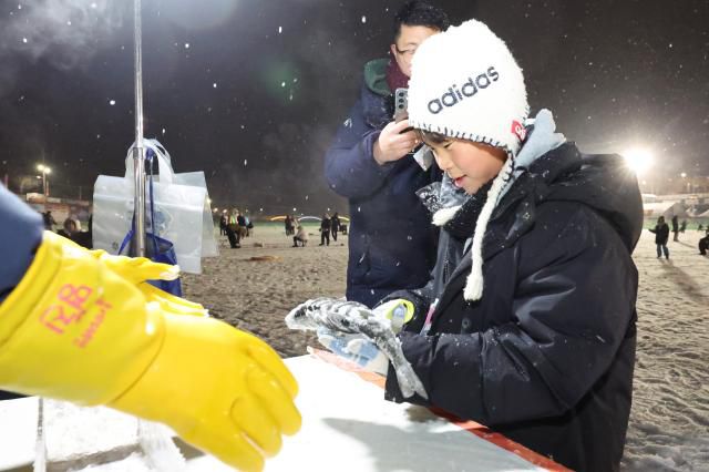 A visitor measures a caught mountain trout at the measuring station at night at the Hwacheon Sancheoneo Ice Festival in Hwacheon, Gangwon Province. Jan. 12, 2026. AJP Han Jun-gu
